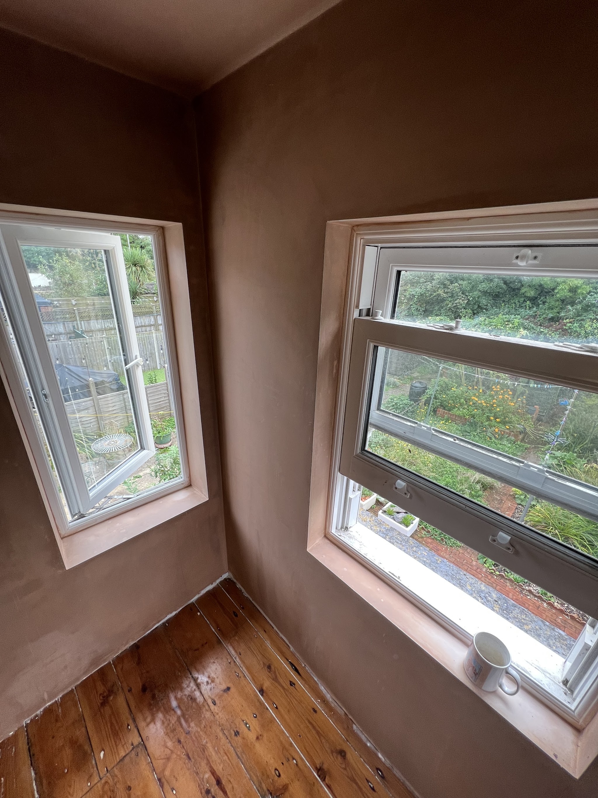 A room corner with two windows, the walls freshly plastered above a wooden floor