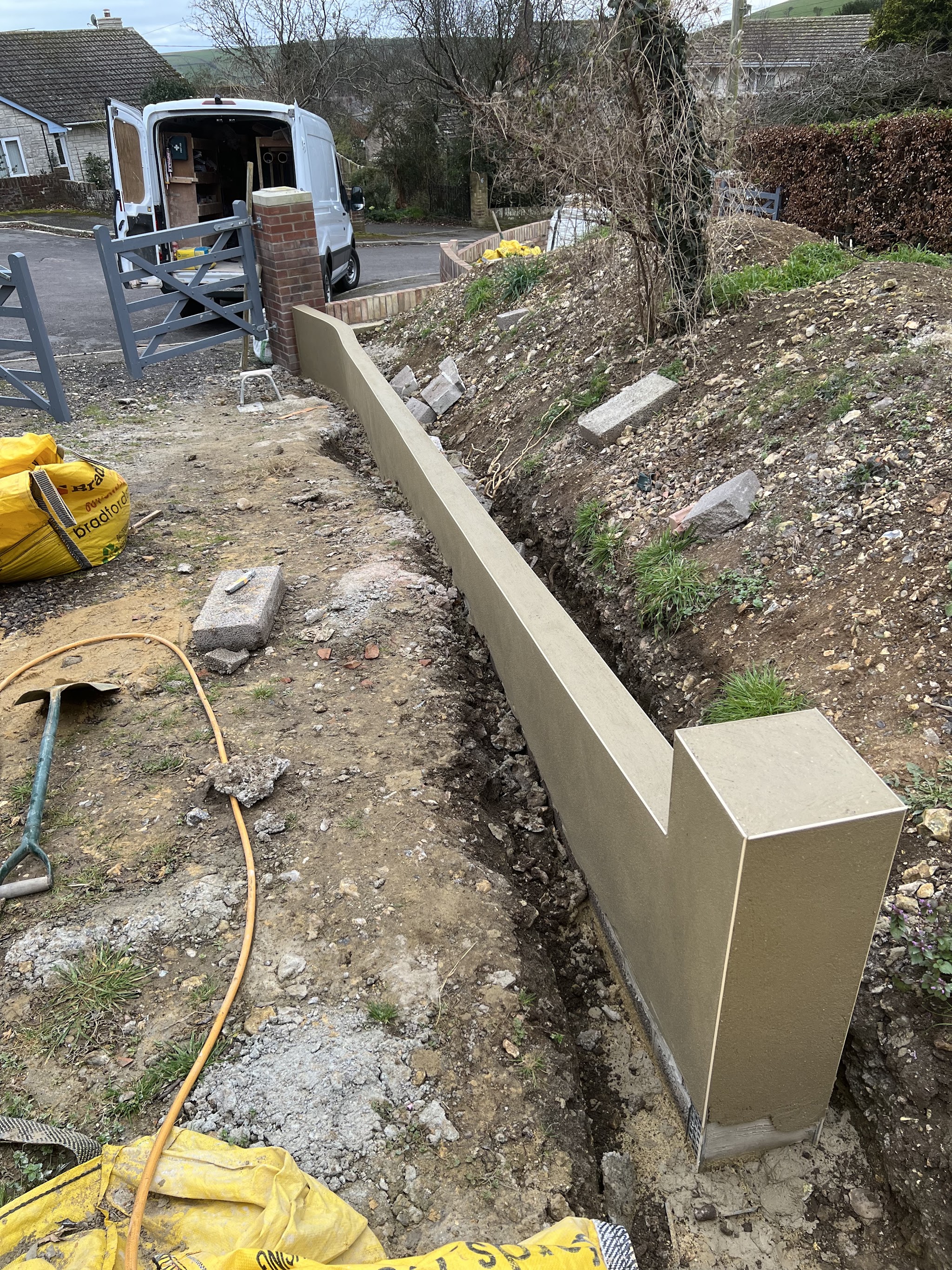 A new rendered retaining wall along a sloping drive, with a grey gate and a van