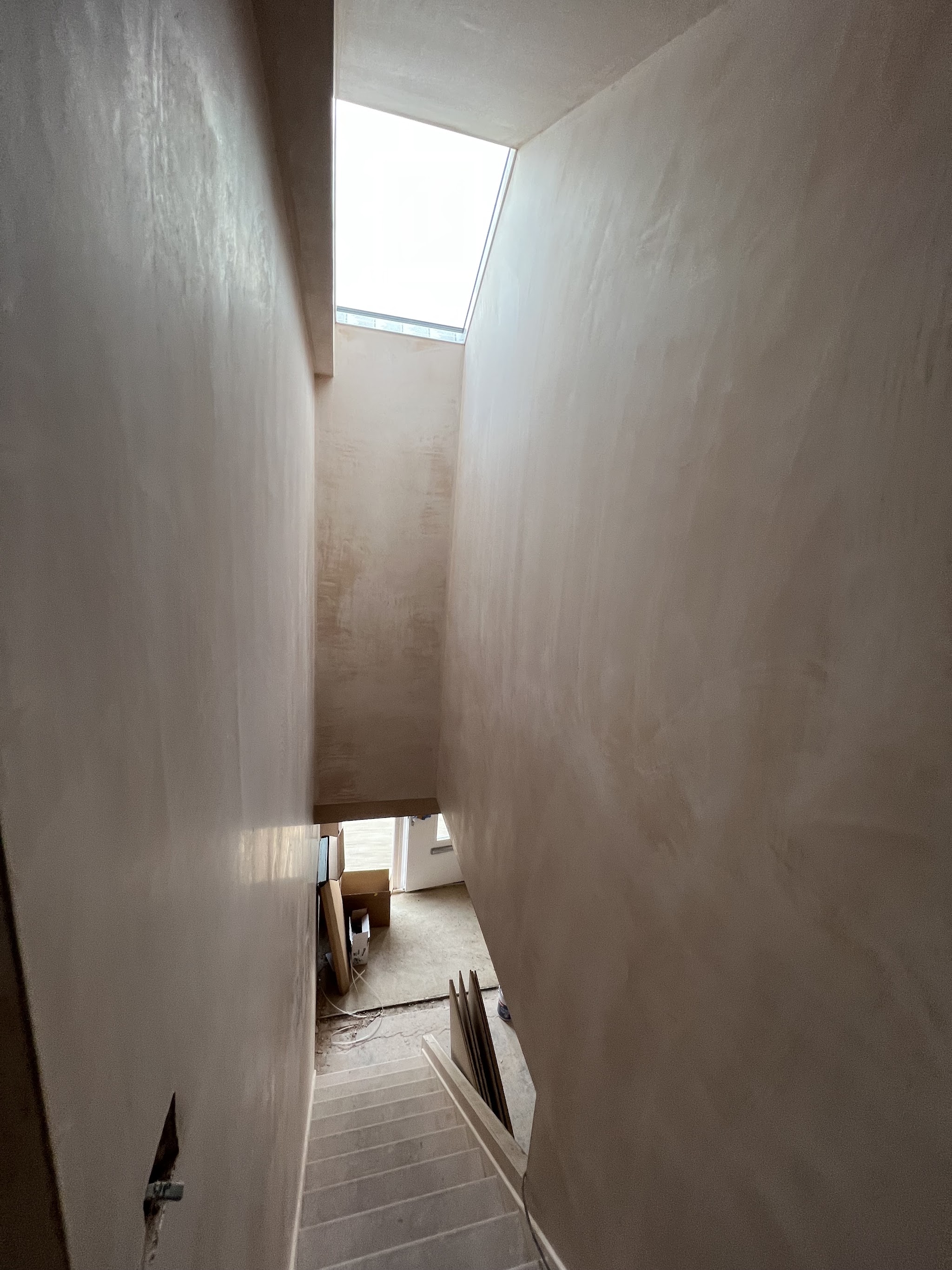 A stairwell with freshly plastered walls under a skylight